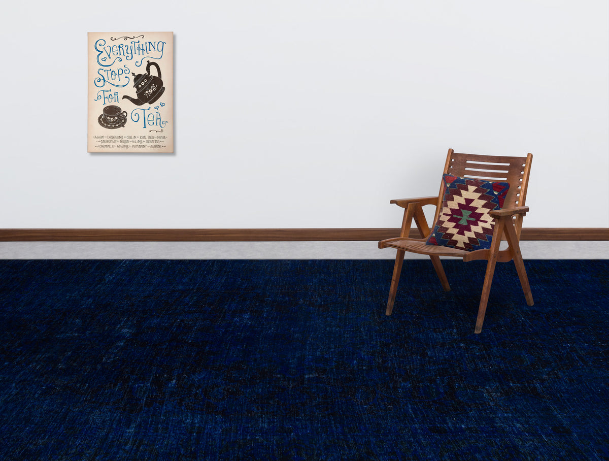 Solid navy blue rug with a subtle distressed texture, styled in a room with a wooden chair and wall art.
