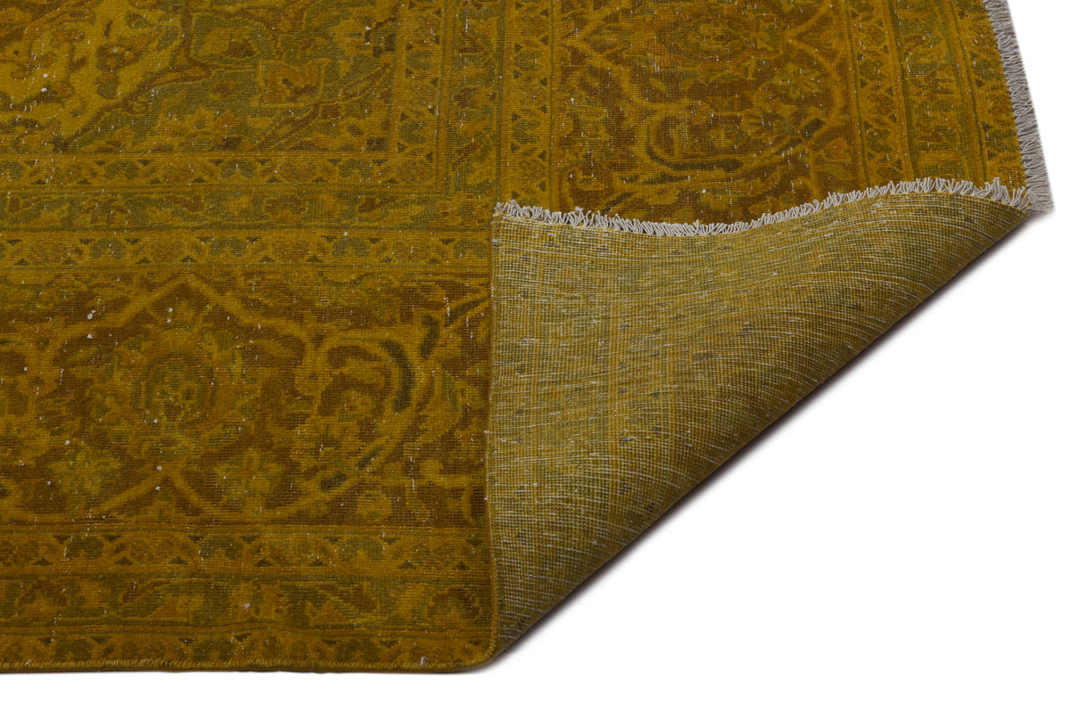 Mustard yellow distressed rug with a traditional medallion pattern and a folded corner showing the woven backing.