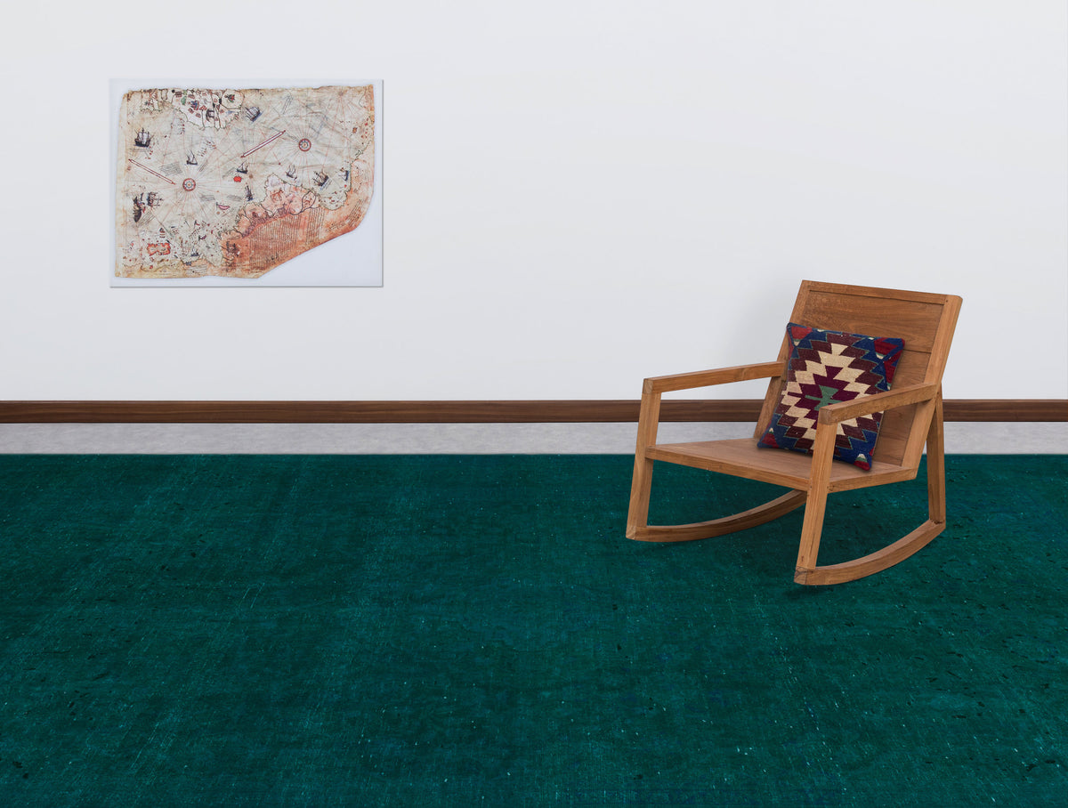 Solid deep teal rug with a distressed texture, styled in a room with a wooden rocking chair and vintage map wall art.