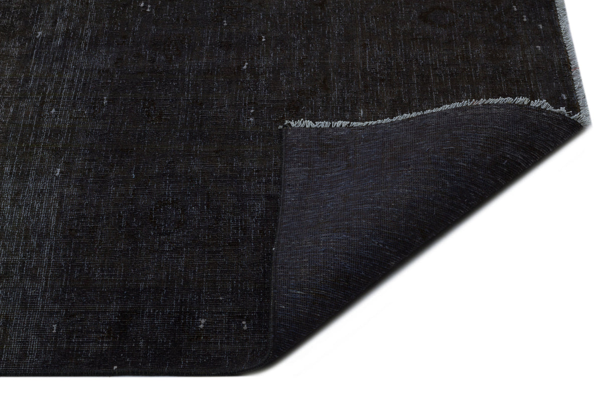 Solid black distressed rug with a folded corner revealing the woven backing and fringe edge.
