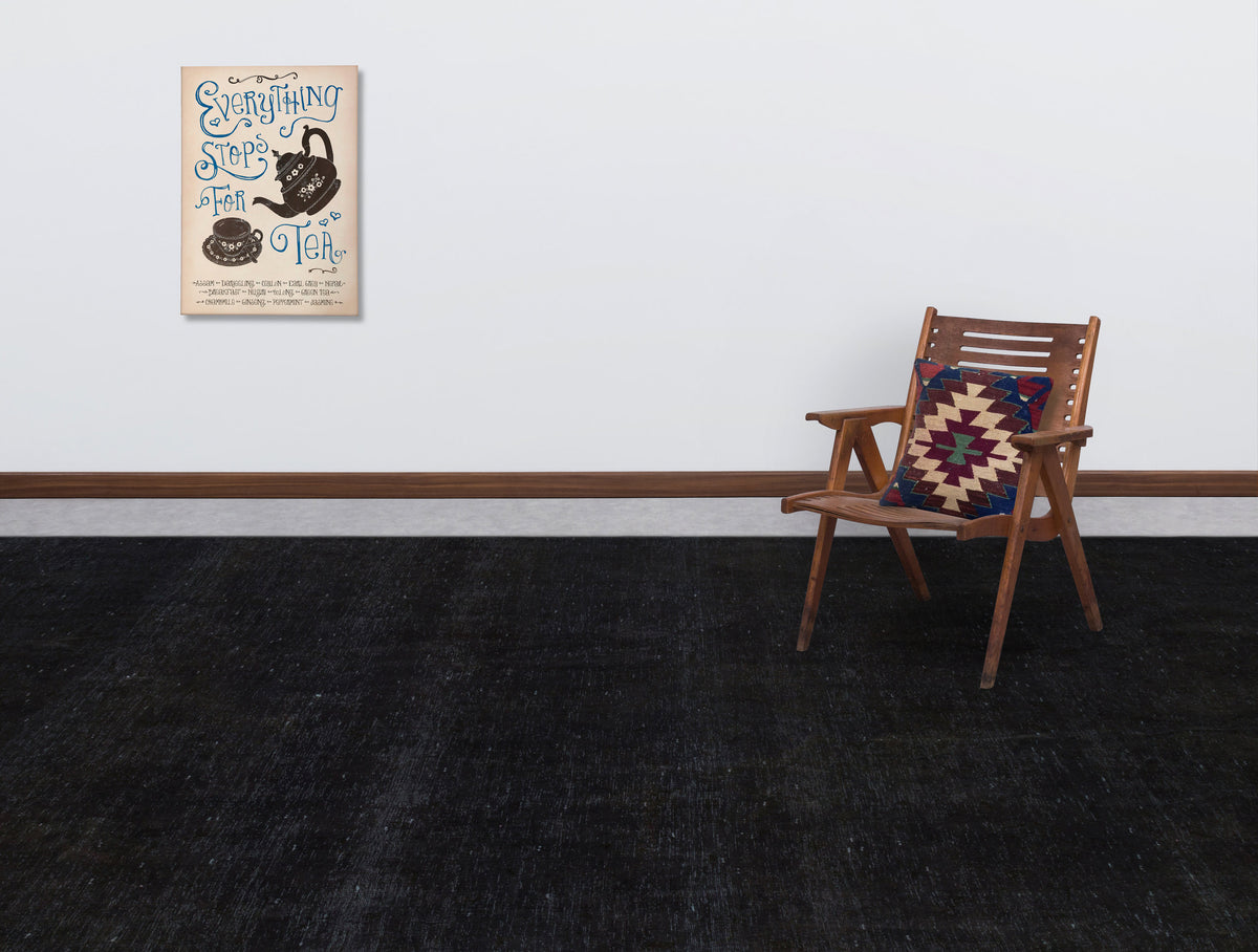 Solid black rug in a room with a wooden chair and tea-themed wall art.