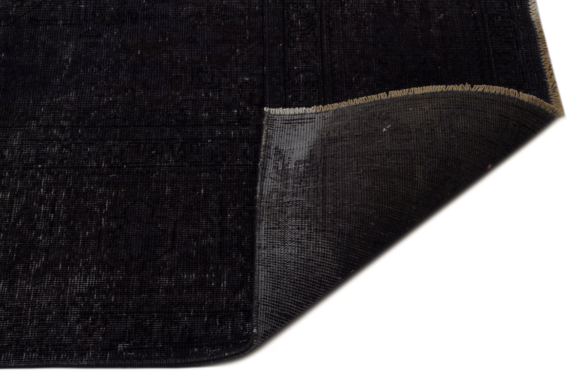Distressed black rug with a folded corner revealing the dark grey woven backing and tan fringe.