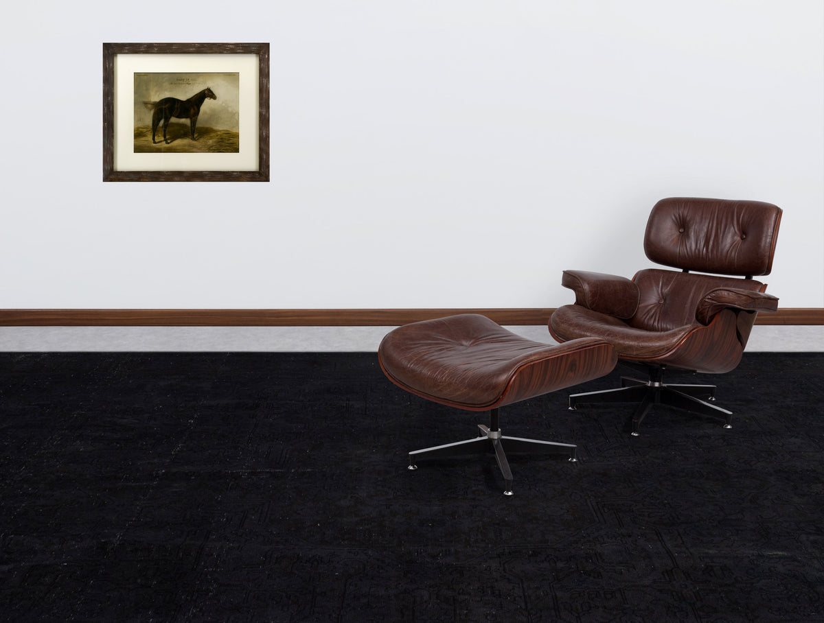 Solid black rug with a subtle tonal traditional pattern, styled in a room with a brown leather lounge chair.