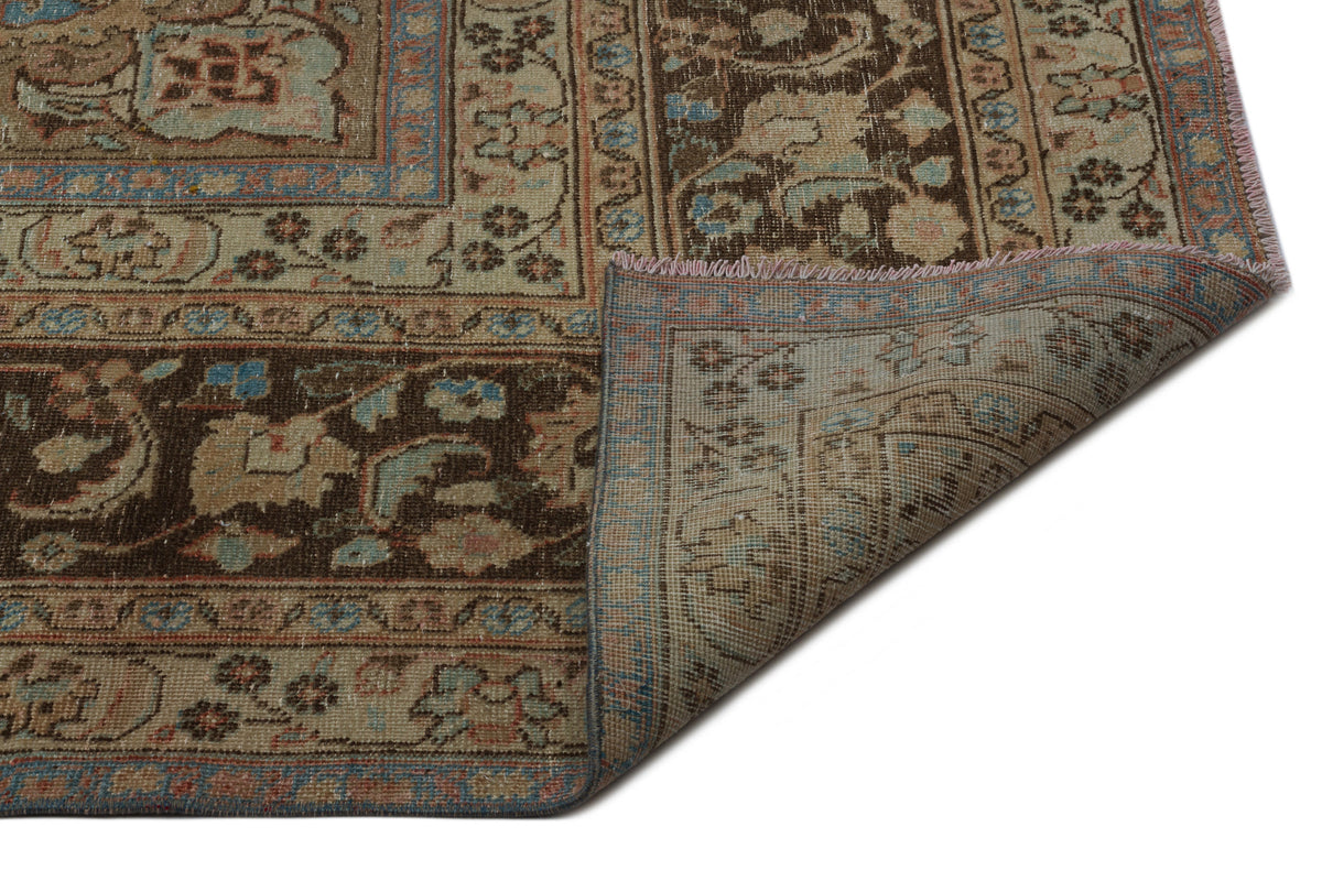 Distressed brown, beige, and blue traditional rug with a floral medallion pattern, shown with a corner folded over.