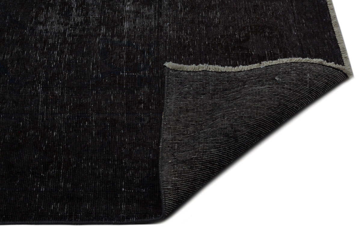 Distressed black and charcoal vintage-style rug with a folded corner revealing a woven backing and fringe edge.