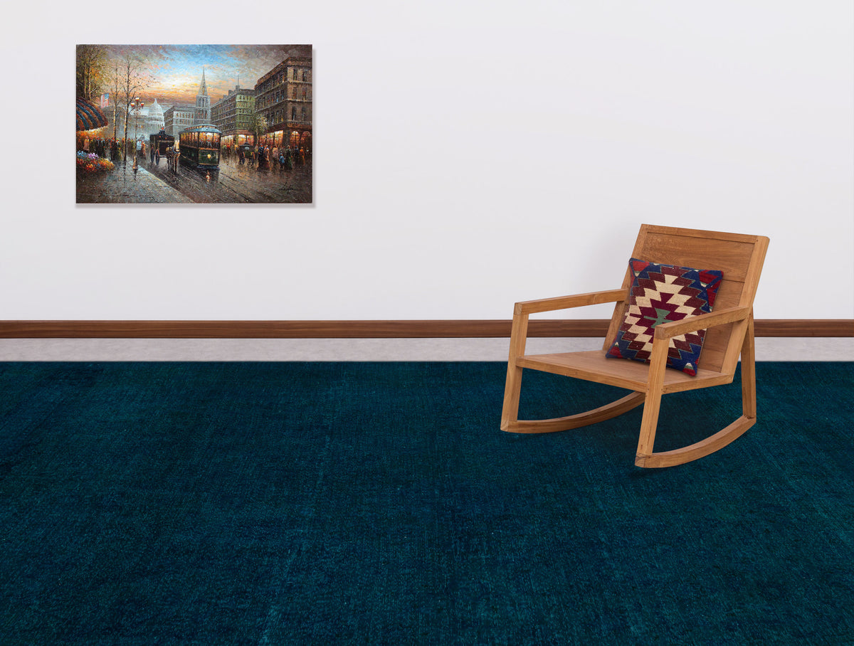 Solid dark teal rug in a room with a wooden rocking chair and wall art.