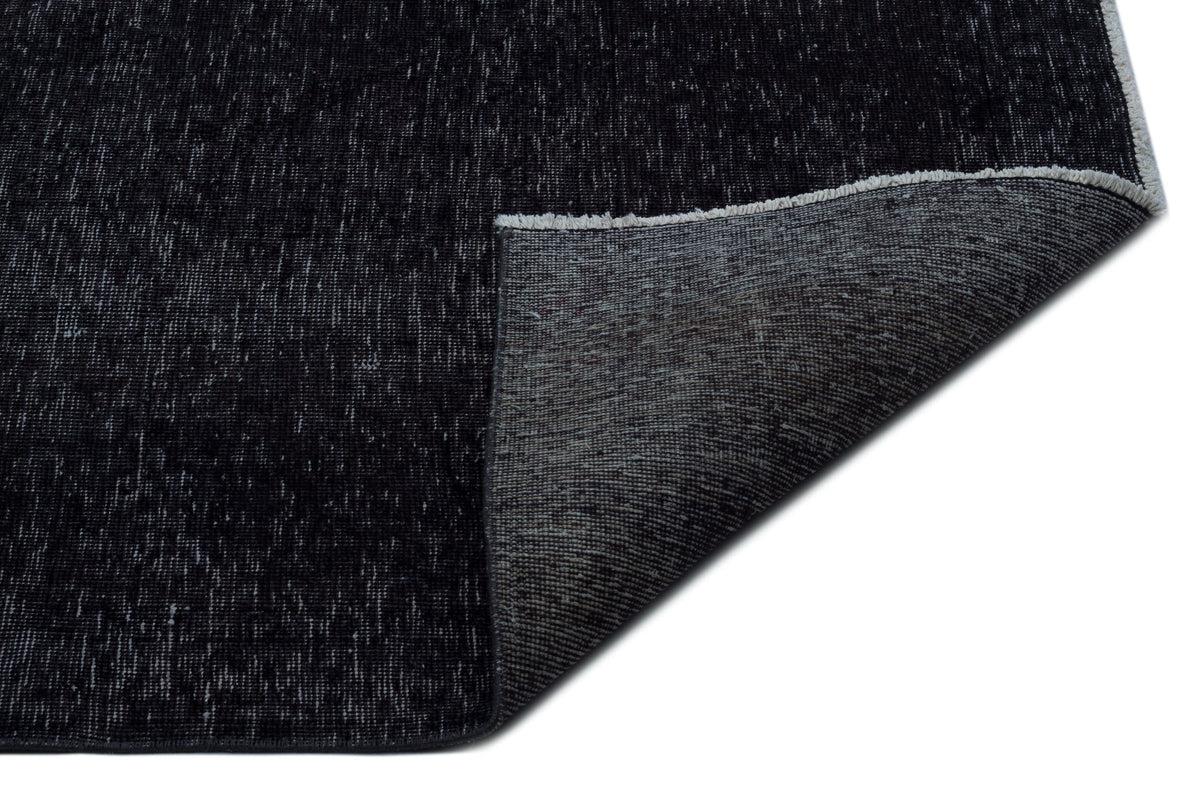 Black distressed-texture rug with a folded corner revealing a grey woven backing on a white background.