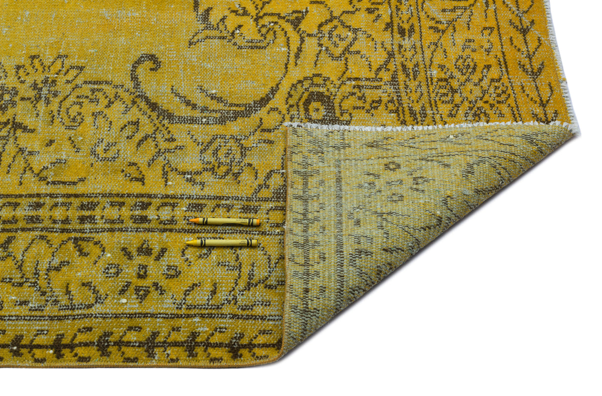 Mustard yellow and brown distressed rug with a traditional floral medallion pattern, shown with a corner folded over.