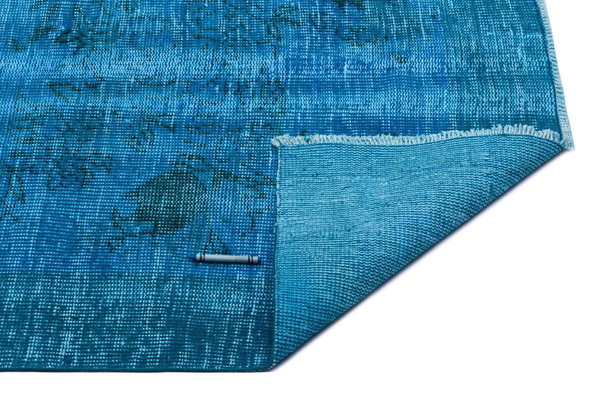 Distressed turquoise blue rug with a faded traditional pattern and a folded corner showing the textured backing.