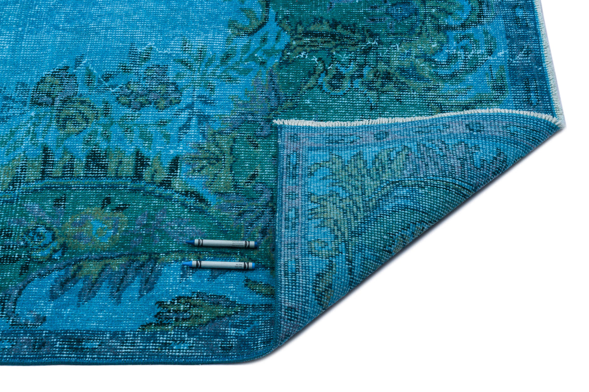 Turquoise and teal distressed traditional rug with a floral medallion pattern, shown with a folded corner on white.