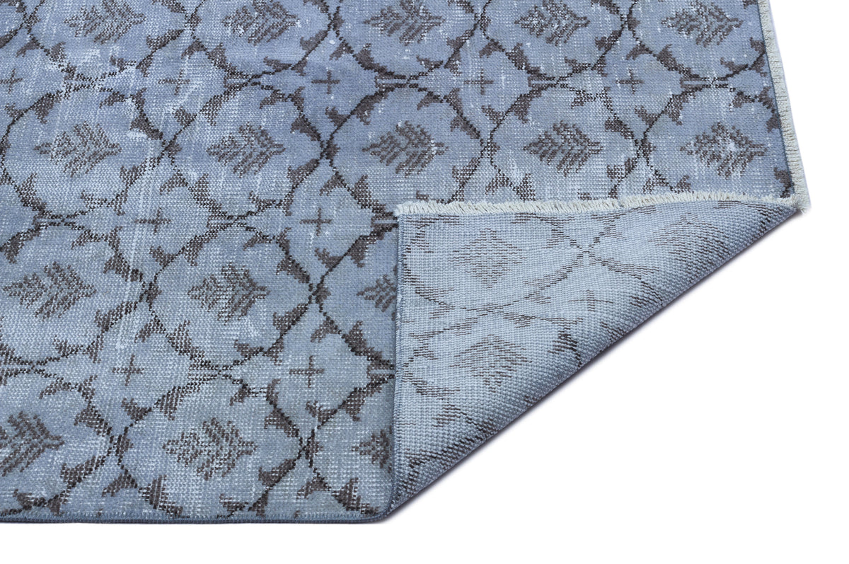 Light blue rug with a dark grey trellis and floral pattern, featuring a folded corner showing the woven backing.