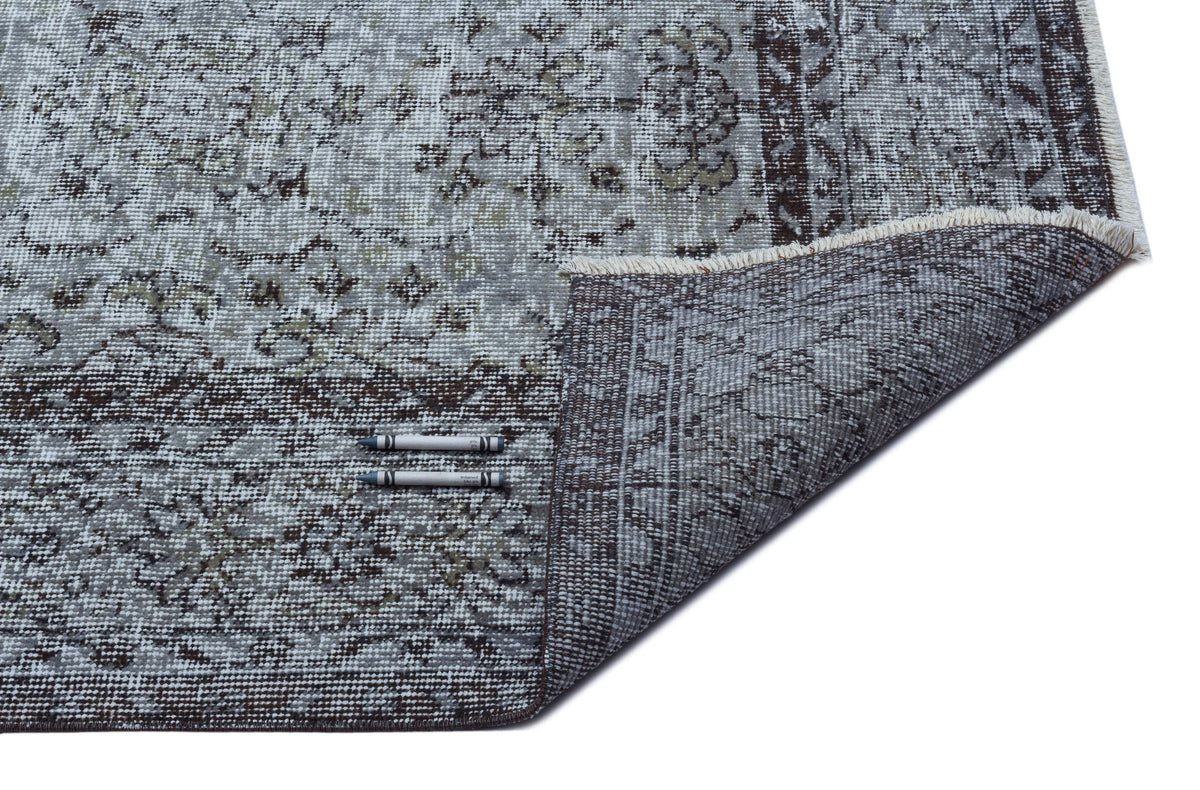 Grey and brown distressed traditional patterned rug with a folded corner showing the woven backing and two crayons.