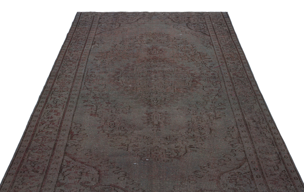 Dark brown and charcoal vintage-style rug with a faded central medallion and intricate border pattern.