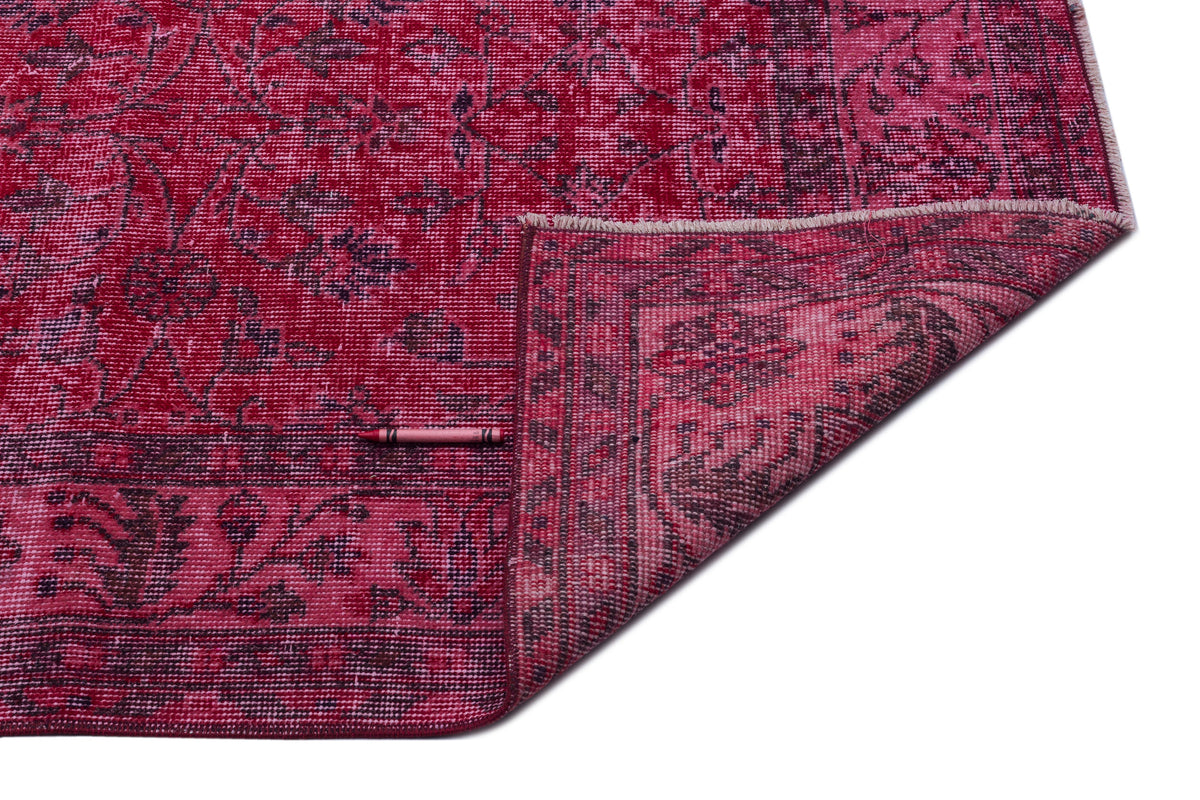 Magenta and dark purple distressed floral rug with a folded corner, isolated on a white background.