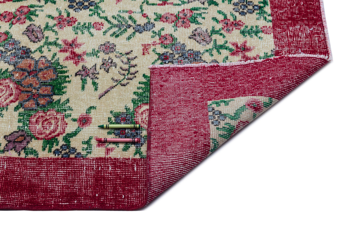 Cream rug with a red border and multi-colored floral pattern, shown with a corner folded over and two crayons.