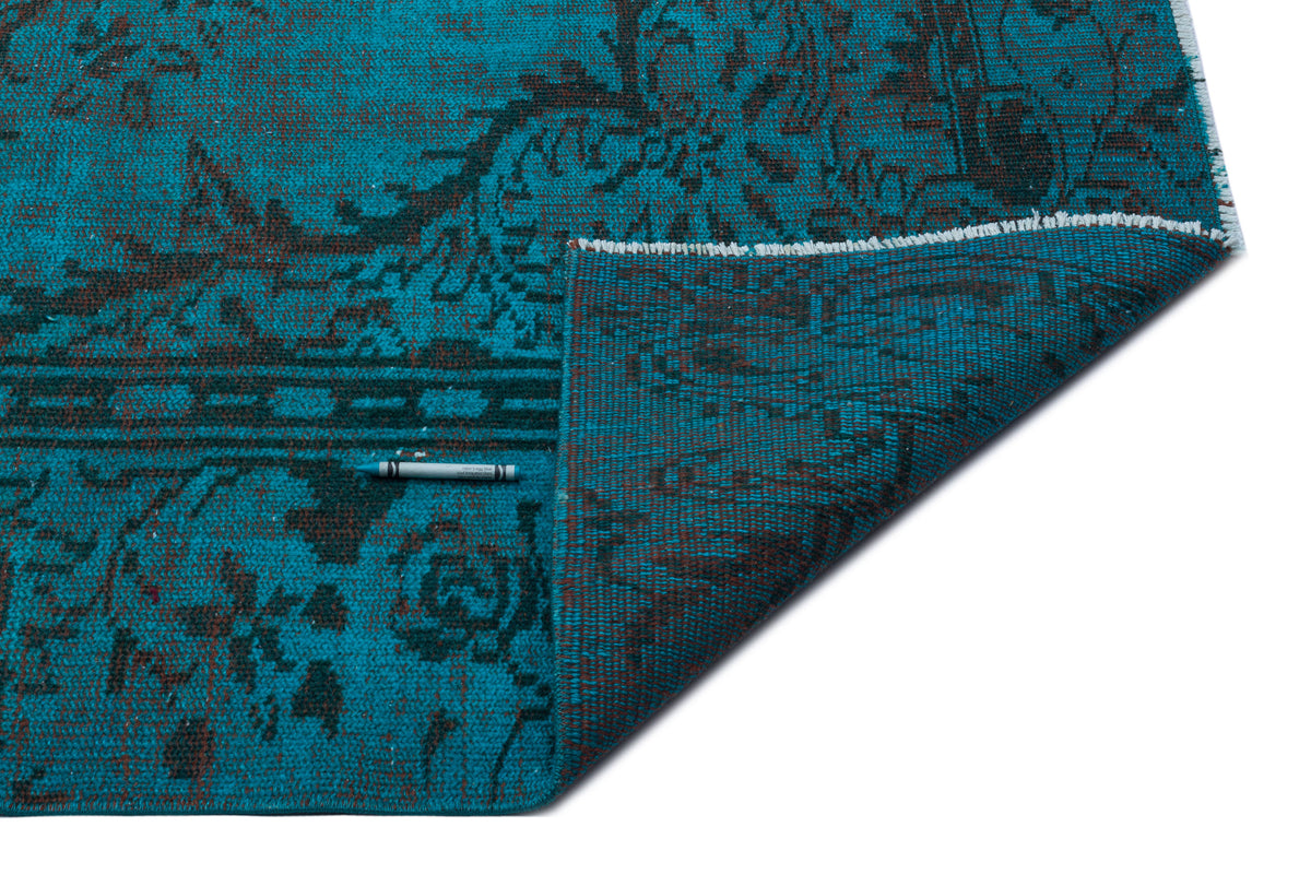Turquoise and dark brown traditional floral pattern rug with a folded corner, isolated on a white background.