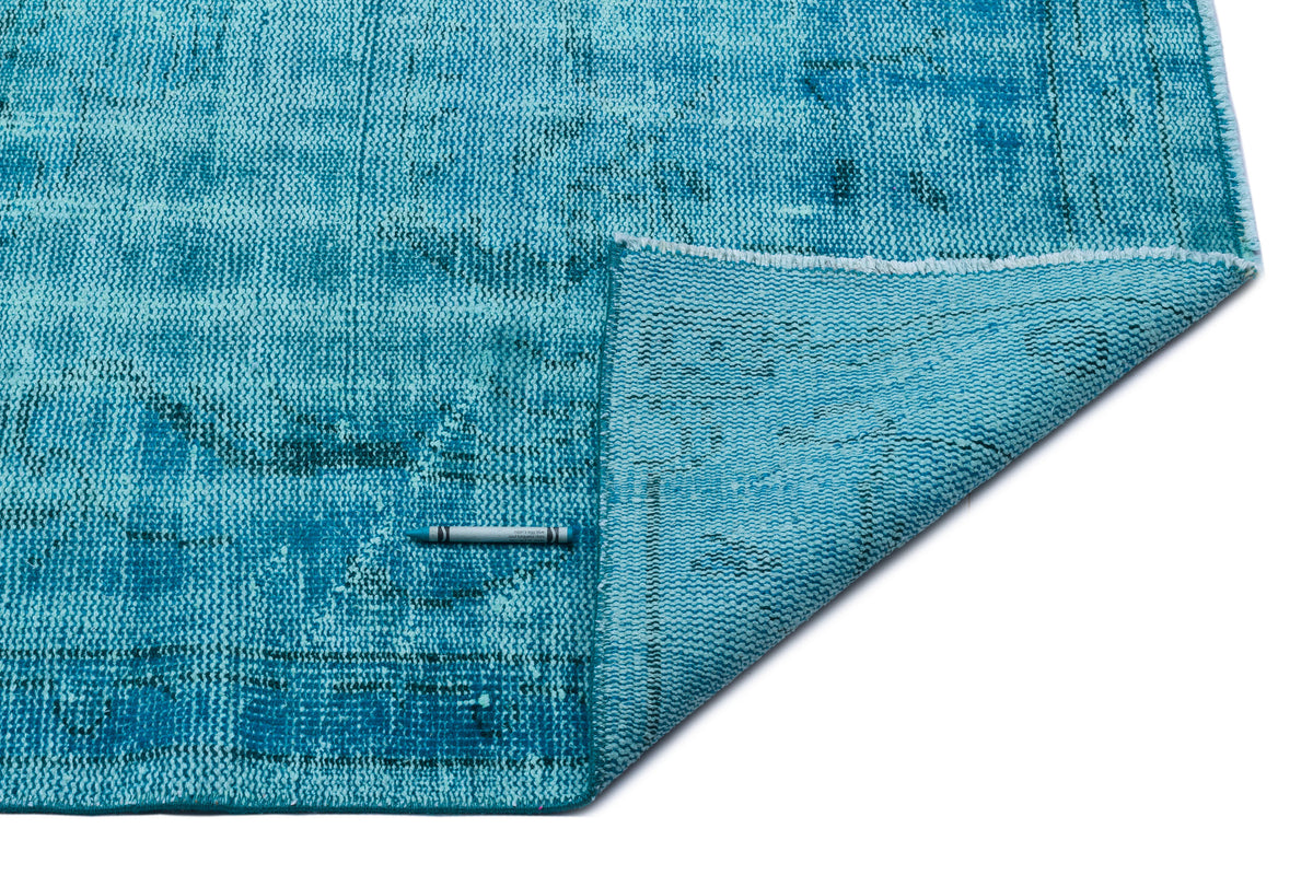 Turquoise distressed area rug with a folded corner, showing a textured weave on a white background.