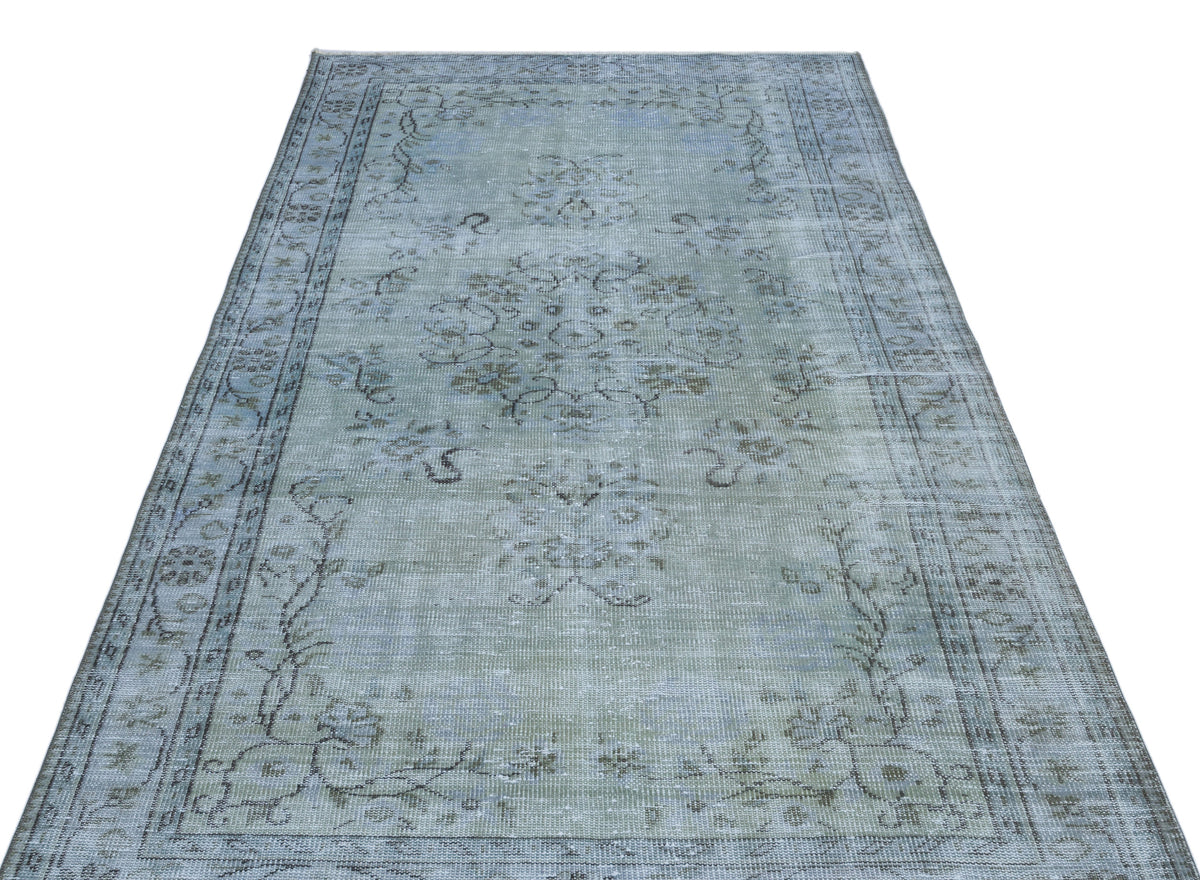 Distressed light blue and grey area rug with a faded central floral medallion and ornate border pattern.