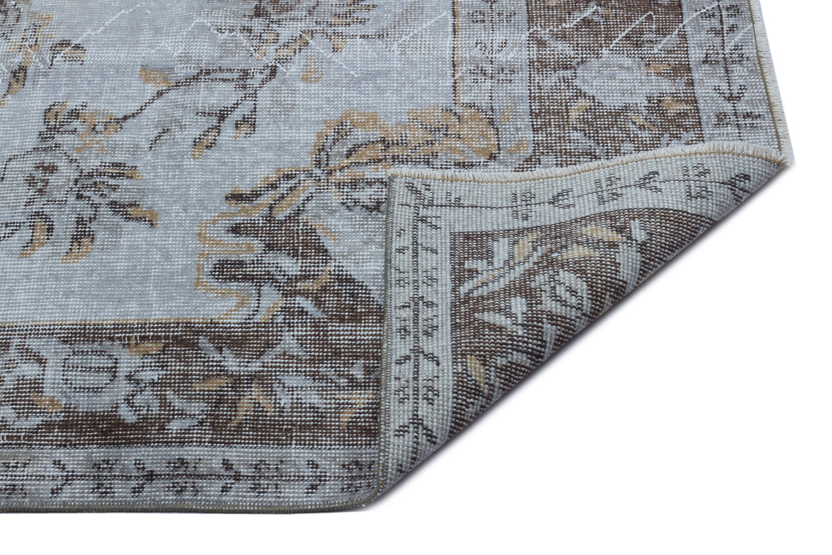 Light blue and brown distressed rug with a traditional floral medallion pattern, shown with a folded corner.