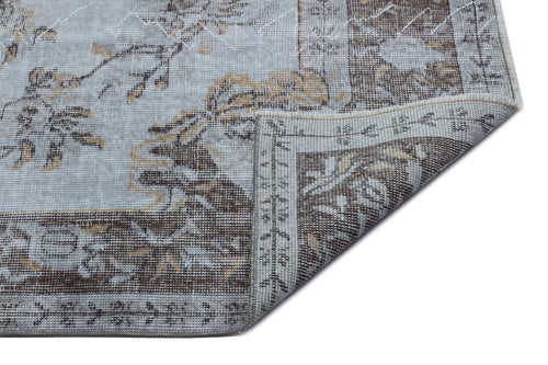 Load image 1 in gallery view. Light blue and brown distressed rug with a traditional floral medallion pattern, shown with a folded corner.