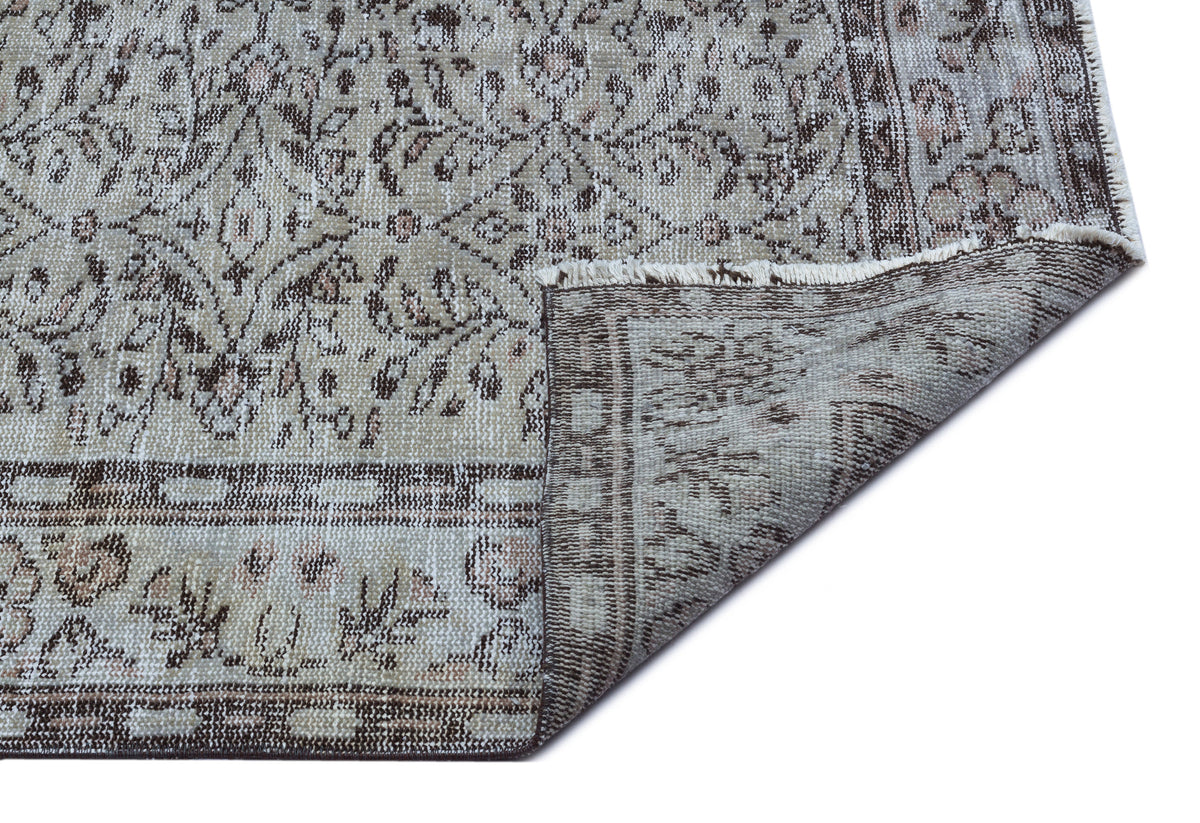 Beige and brown distressed traditional rug with a floral medallion pattern, shown with a corner folded over.
