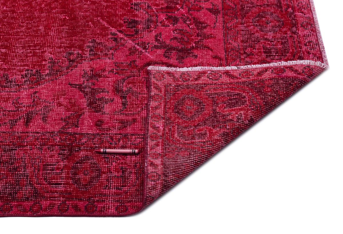 Deep red distressed rug with a dark floral medallion pattern and a folded corner, isolated on a white background.