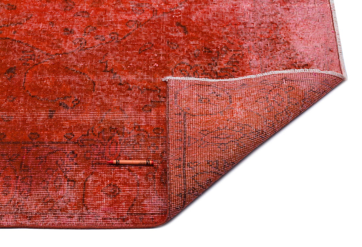 Distressed red and pink vintage-style rug with a faded floral medallion pattern, shown with a corner folded over.
