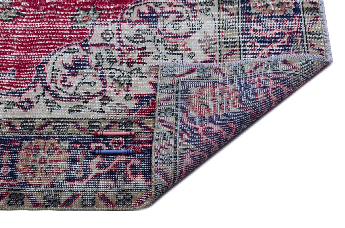 Distressed red, navy, and cream traditional medallion rug with a folded corner, shown on a white background.