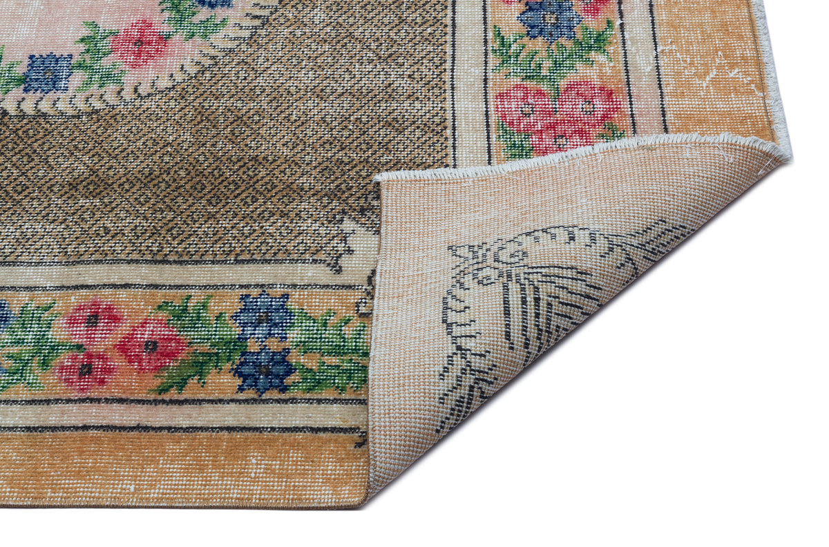 Tan and brown vintage-style rug with floral borders and a corner folded over to reveal the woven backing.