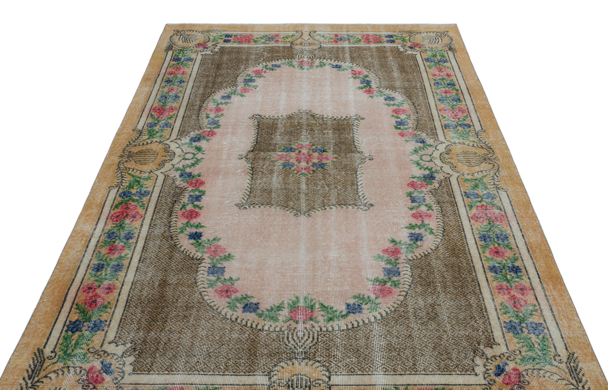 Distressed brown and pink vintage-style rug with a central floral medallion and decorative floral border.