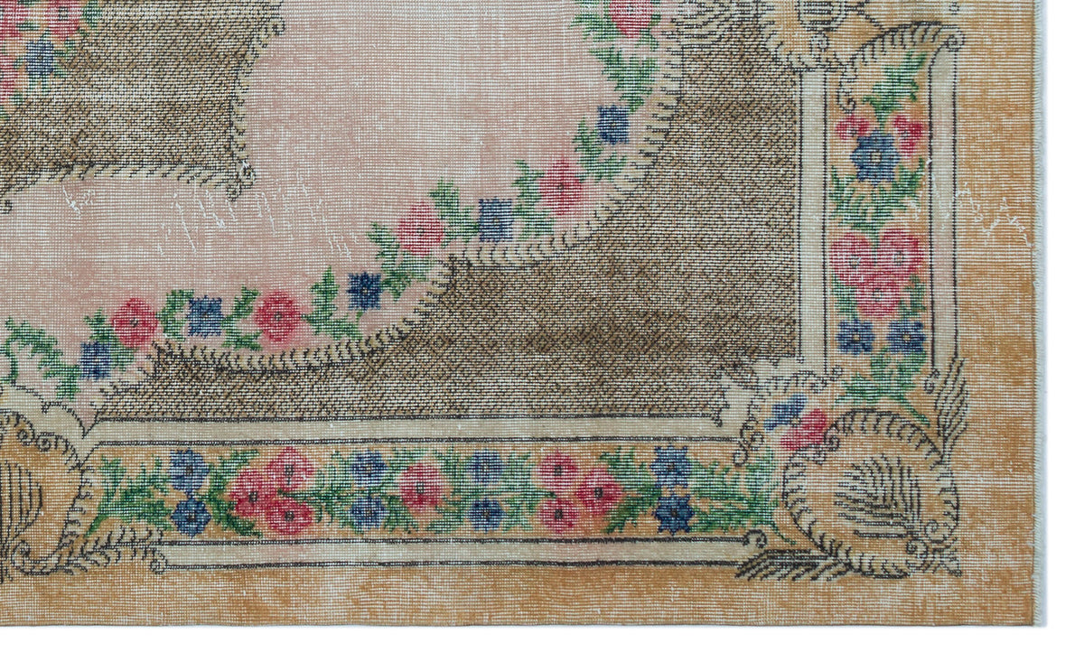 Vintage-style rug with a pink central field, tan border, and floral garland pattern in red, blue, and green.