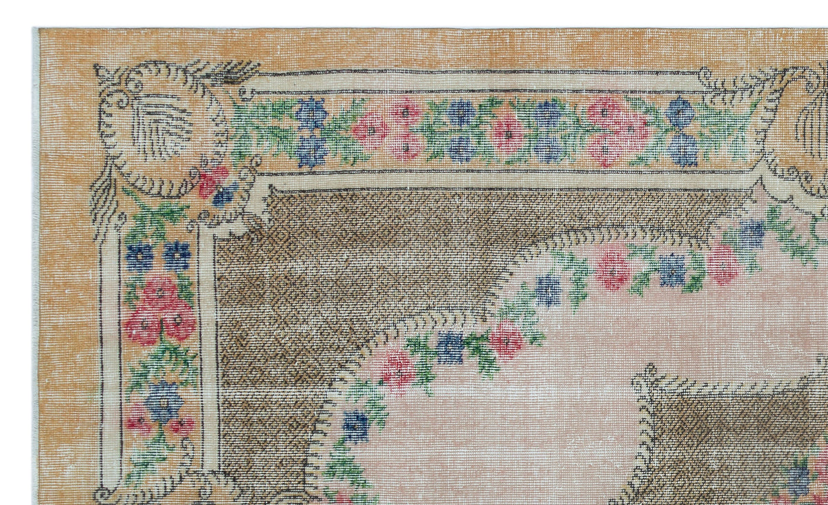 Distressed tan rug with a floral border in pink, blue, and green, featuring a central medallion design.