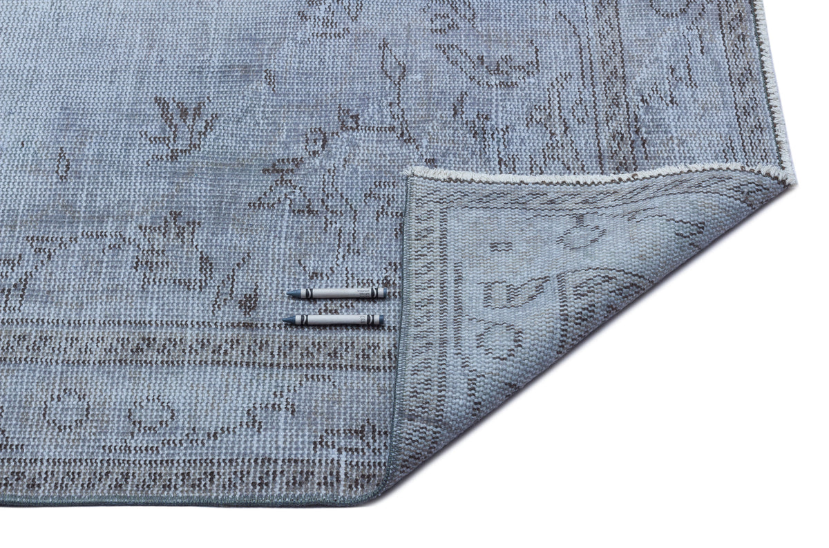 Light blue and grey distressed traditional rug with a floral medallion pattern, shown with a corner folded over.