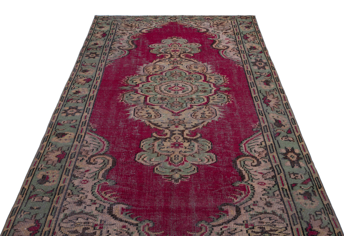 Magenta vintage-style rug with a central sage green and beige floral medallion and a distressed border.