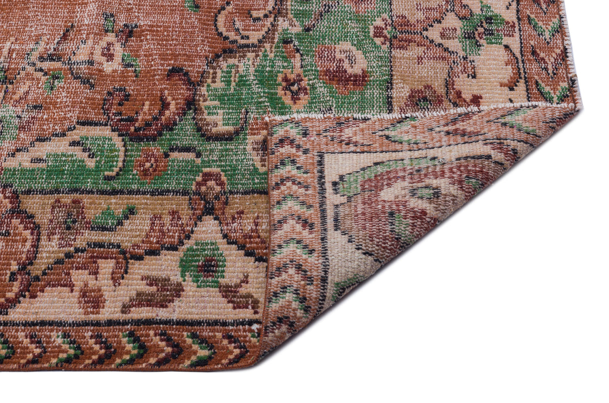 Distressed terracotta, green, and beige vintage-style rug with a floral medallion pattern, shown with a folded corner.