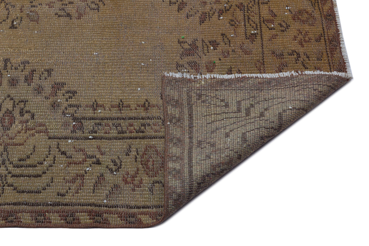 Distressed brown and tan vintage rug with a faded floral medallion pattern and a folded corner showing the backing.