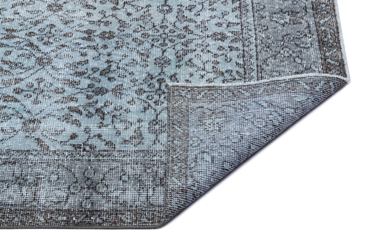 Light blue and charcoal grey traditional rug with a distressed floral pattern, shown with a folded corner.