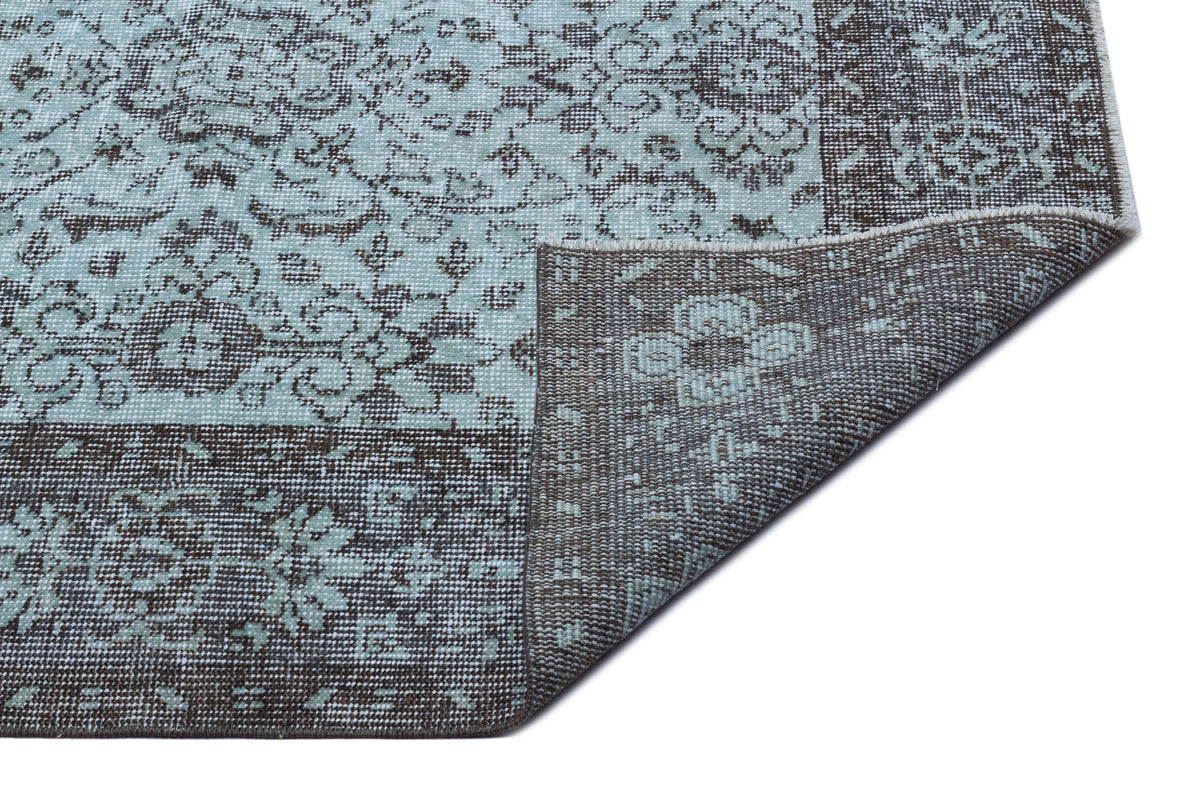 Light blue and dark brown rug with a distressed floral medallion pattern, shown with a corner folded over.