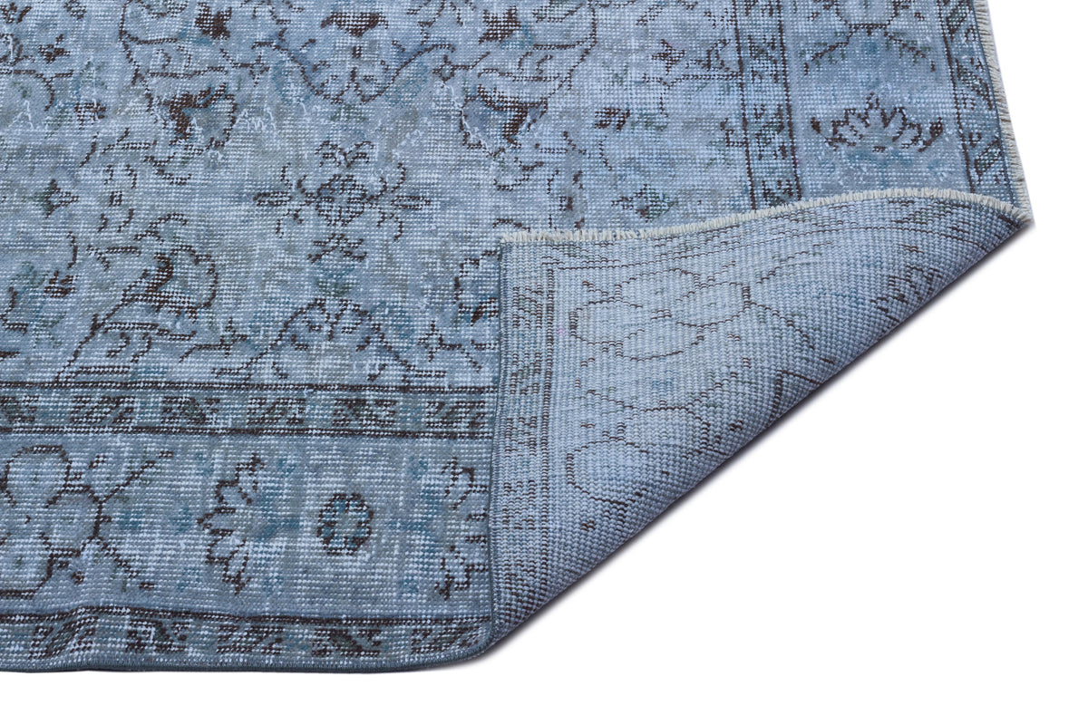 Light blue and grey distressed rug with a traditional floral medallion pattern, shown with a folded corner.
