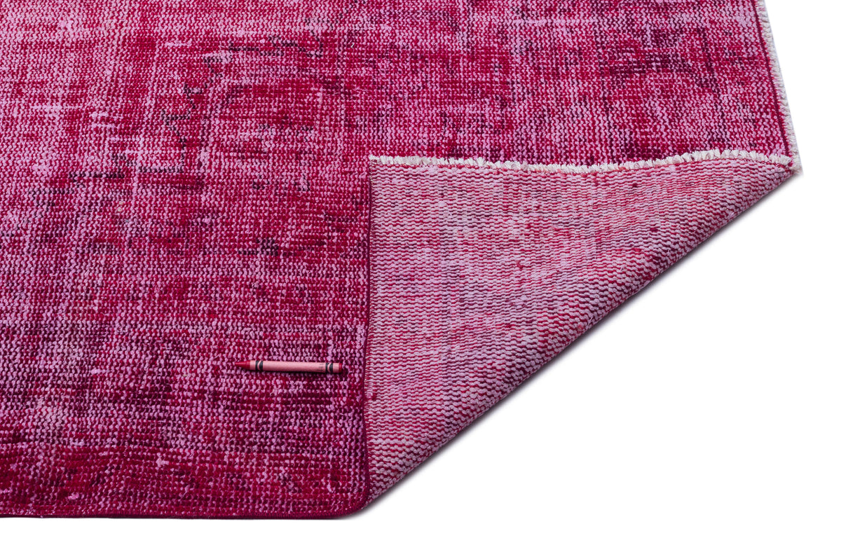Distressed magenta and pink overdyed rug with a folded corner revealing the woven backing and a pink crayon for scale.