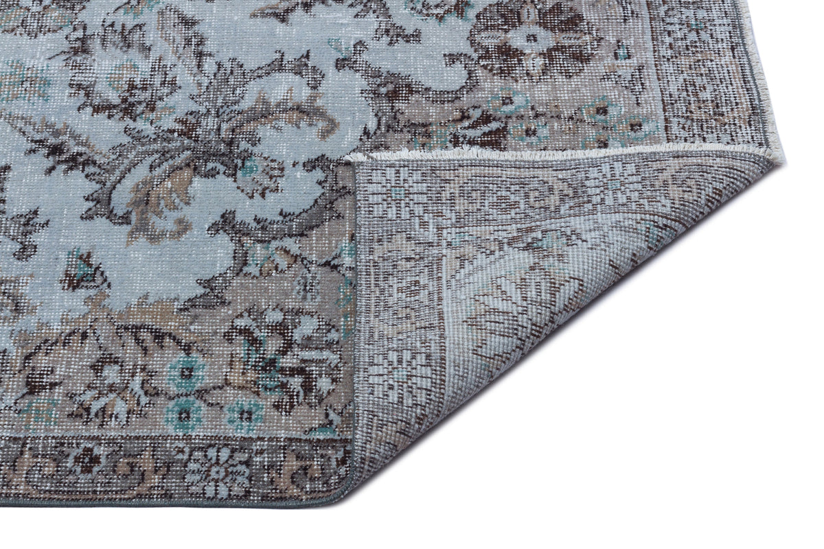 Light blue and brown distressed traditional rug with a floral medallion pattern, shown with a corner folded over.