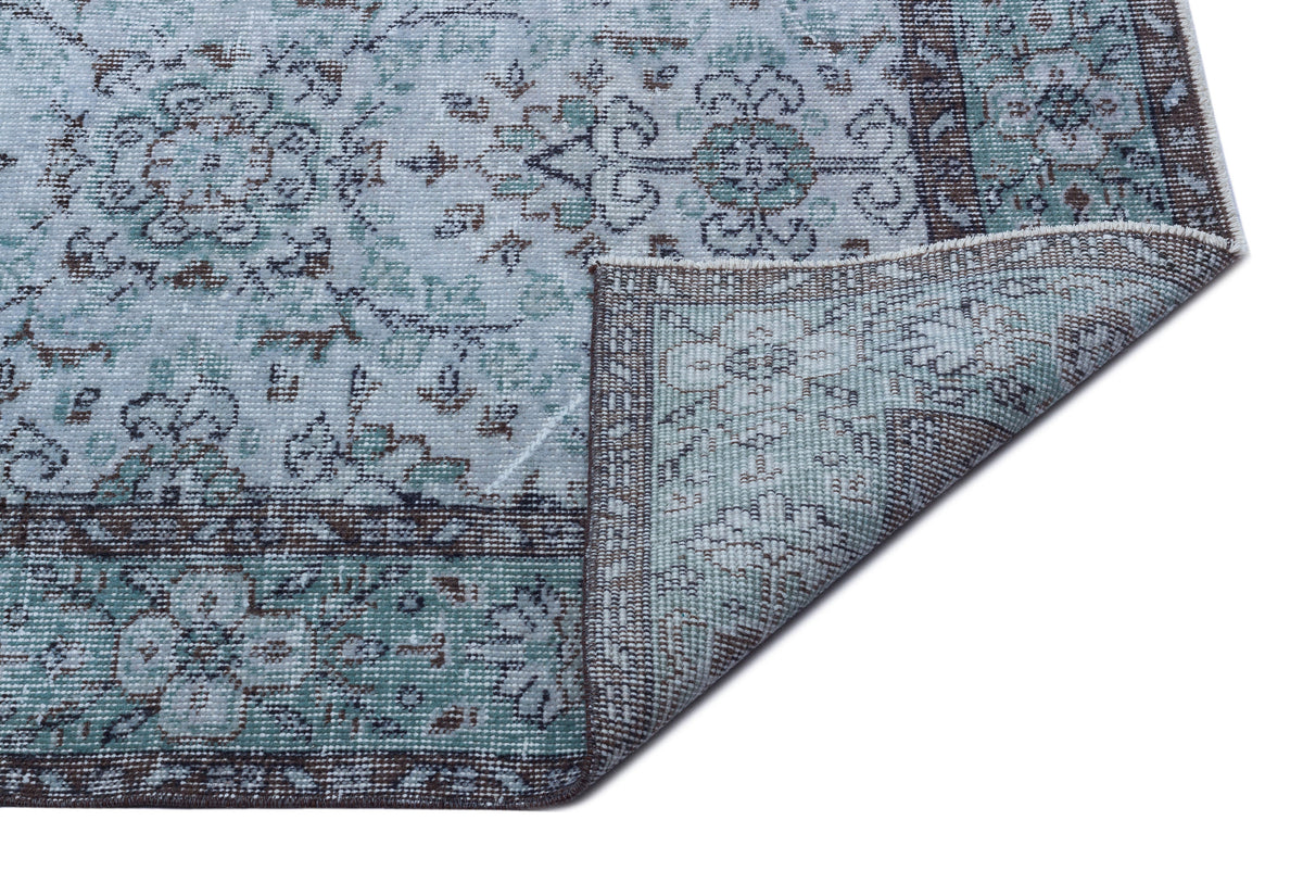 Light blue and brown vintage-style rug with a floral medallion pattern, shown with a corner folded over.
