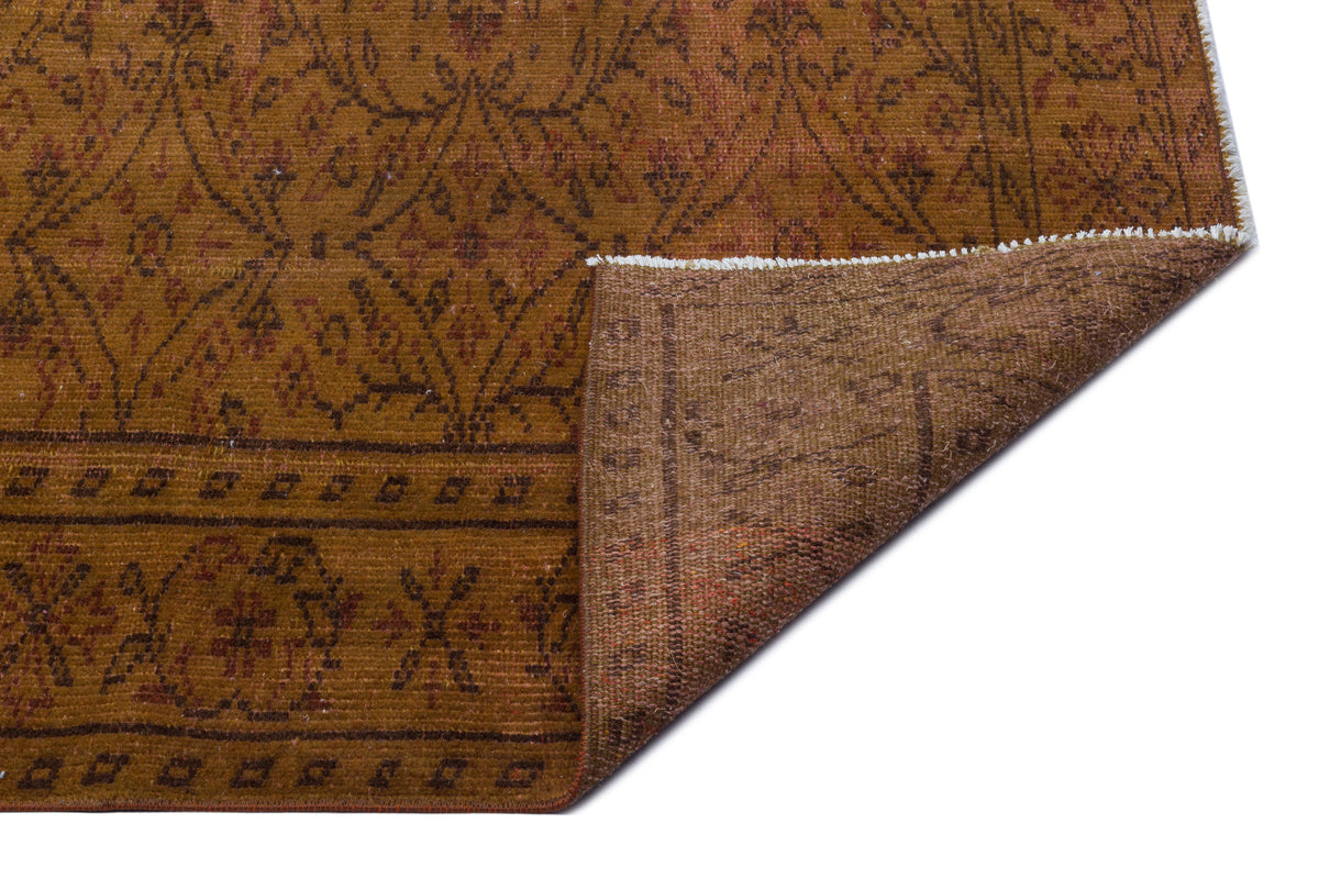 Ochre and brown traditional rug with a geometric floral pattern, shown with a corner folded over on a white background.