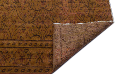 Load image 1 in gallery view. Ochre and brown traditional rug with a geometric floral pattern, shown with a corner folded over on a white background.