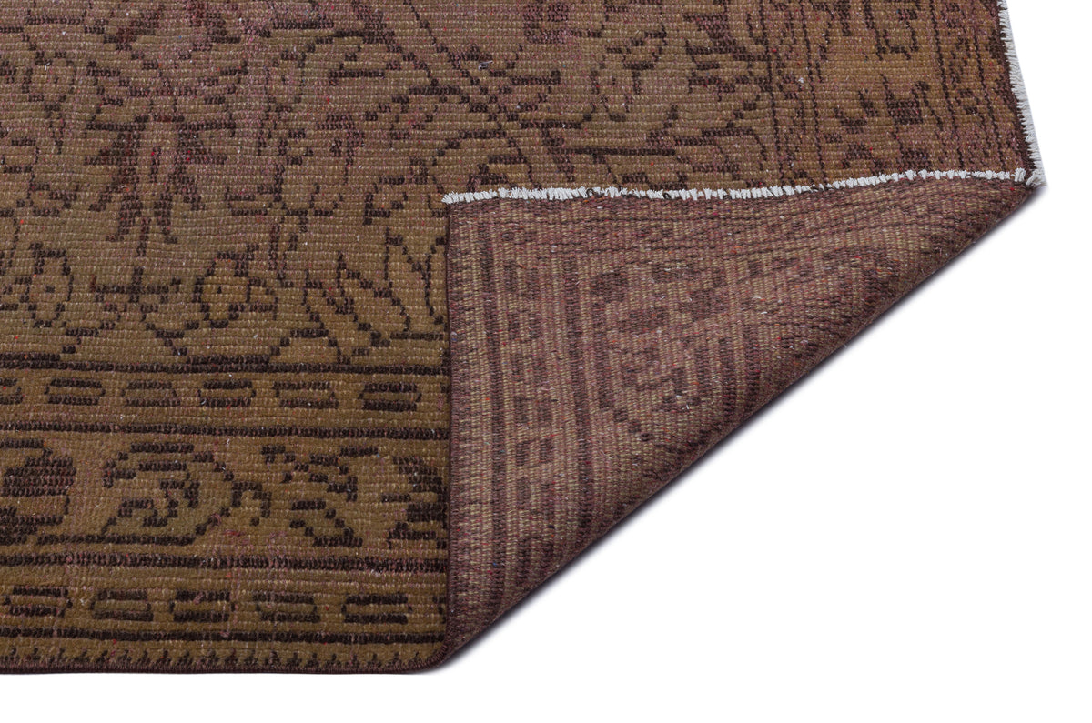 Brown and dark brown vintage-style rug with a traditional floral pattern and a folded corner showing the underside.