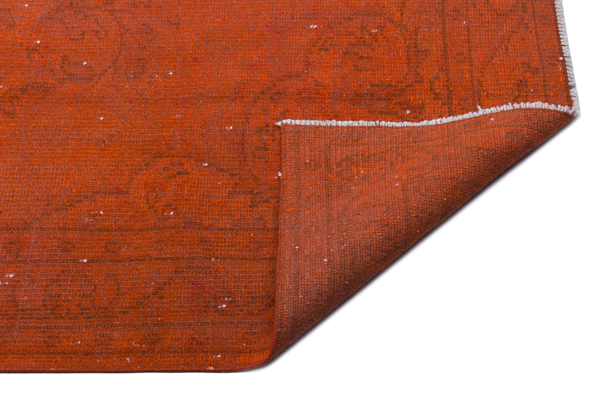 Burnt orange rug with a subtle distressed pattern and a folded corner showing the weave texture on a white background.