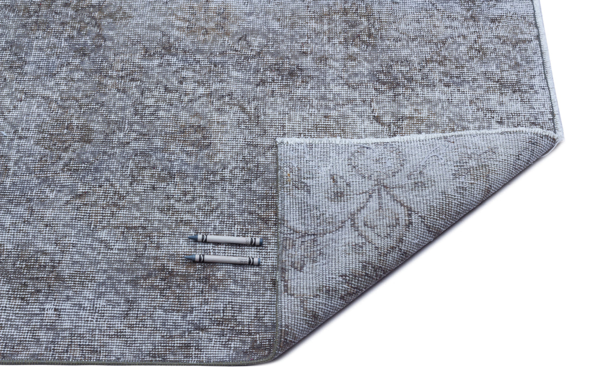 Grey and taupe distressed rug with a faded floral medallion pattern, shown with a corner folded over on white background.