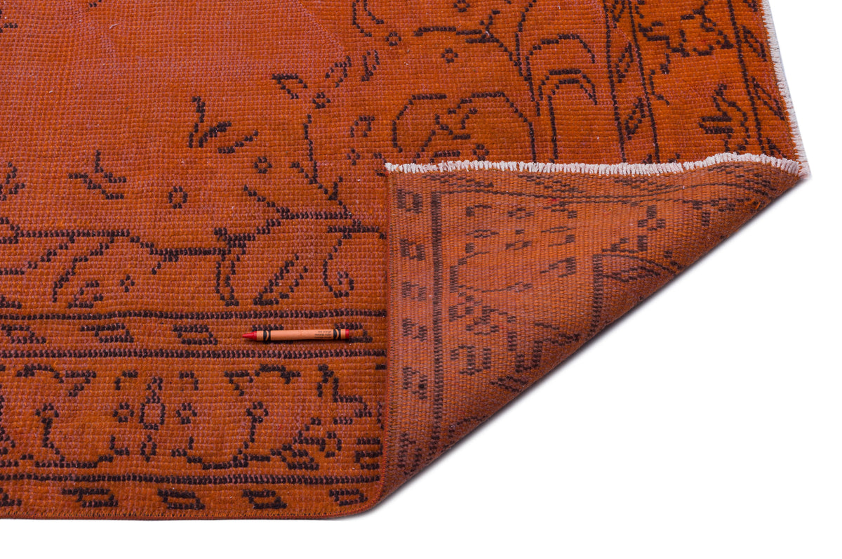 Burnt orange rug with a dark brown floral pattern and a folded corner showing the underside, isolated on white.