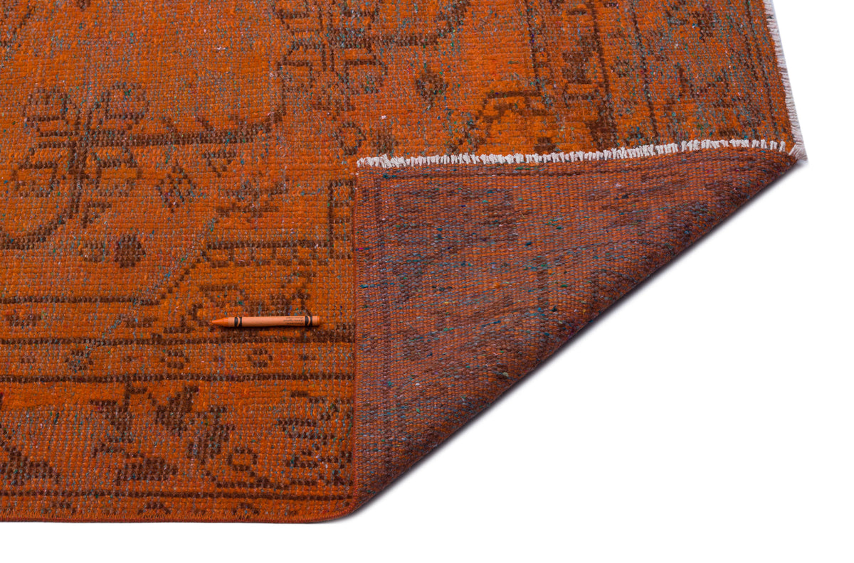 Burnt orange rug with a distressed traditional pattern and a folded corner showing the dark brown textured backing.