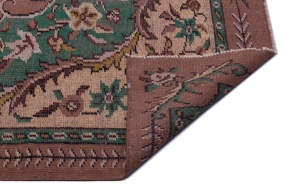 Brown and green traditional floral patterned rug with a folded corner revealing the woven backing.
